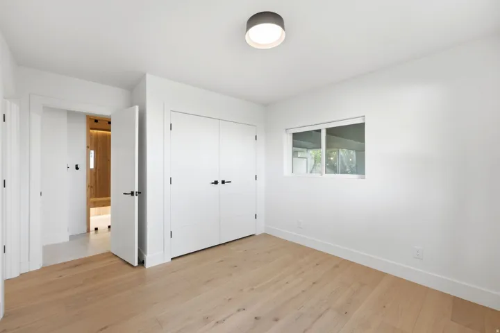 Light wood-finish flooring, white walls, built-in closet with double doors, and a rectangular window
