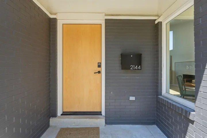 Brick exterior with a contemporary light wood-finish entry door, matte black door hardware, and an expansive window