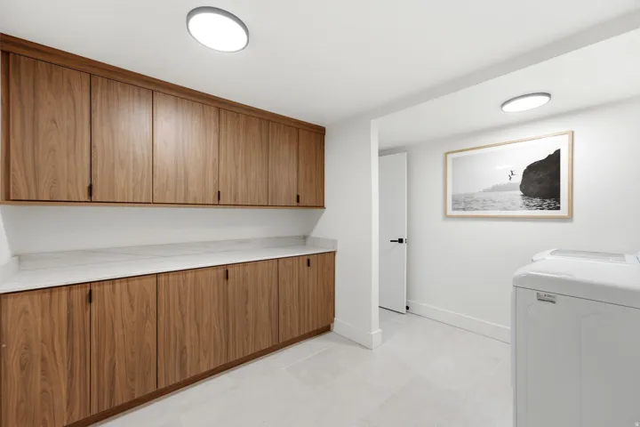 Extensive wood-finish cabinetry with matte black hardware, white countertops, and light tile flooring