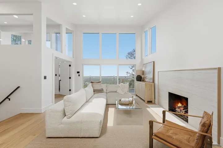Vaulted ceilings, large windows, wood-finish flooring, white fireplace surround, and recessed lighting