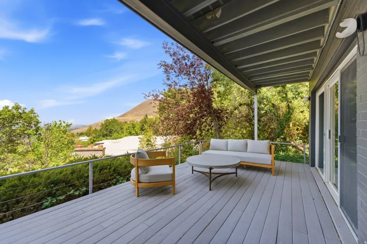 Covered outdoor deck with light gray wood-finish flooring, white sliding glass doors, and a cable railing system