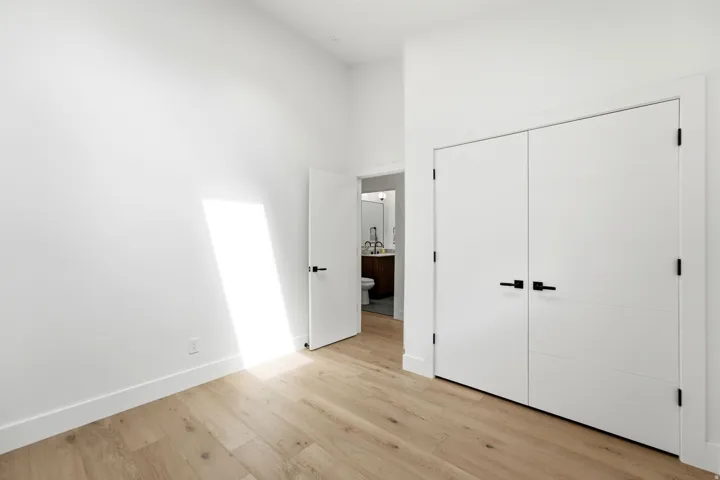 Light wood-finish flooring, white walls, and modern white doors with matte black hardware