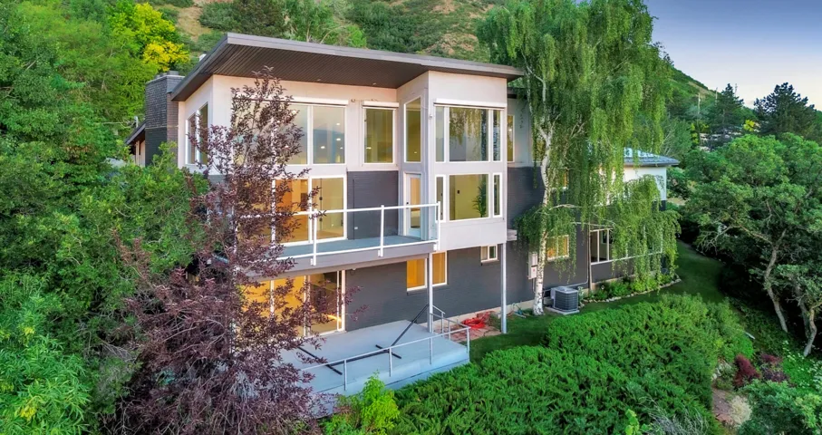 Multi-level architectural design featuring expansive window walls, two exterior balconies with glass railings, a flat roofline, and a stucco and panel exterior
