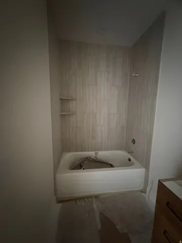 White bathtub with a chrome-finish faucet, surrounded by light-toned rectangular wall tiles, and built-in shelving