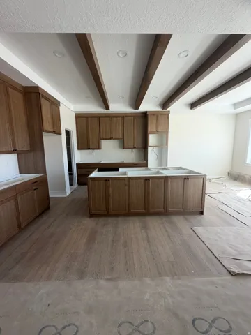 Kitchen featuring wood-finish flooring, recessed lighting, wood ceiling beams, wood-finish cabinetry, and an island with an integrated sink