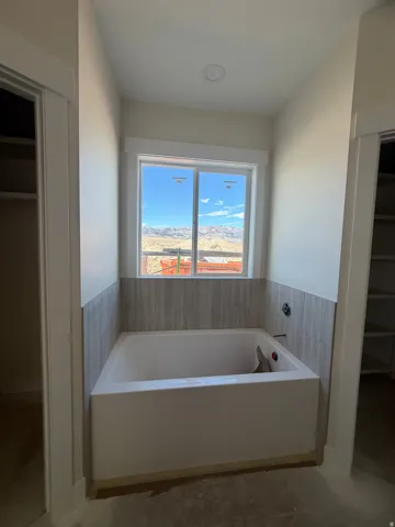 Recessed lighting, tile shower surround, built-in bathtub, window with mountain backdrop, and two adjacent closet openings