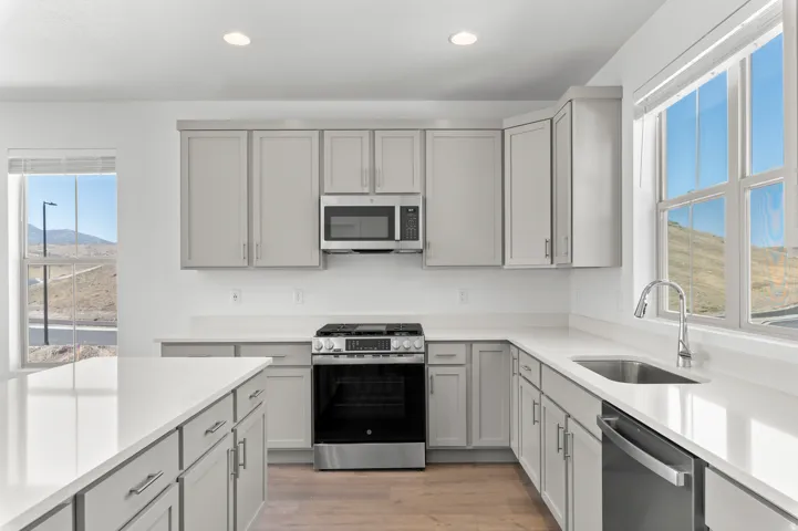 Kitchen featuring light-toned cabinetry, stainless steel appliances, white countertops, and wood-finish flooring
