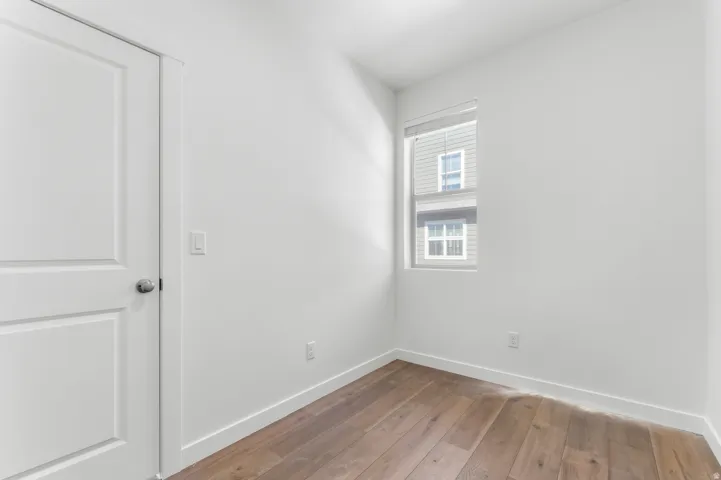 White paneled door, wood-finish flooring, white walls, and a window with blinds