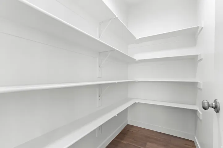 White shelving with wall-mounted brackets, wood-finish flooring, and a brushed nickel doorknob