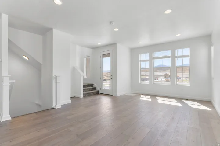 Spacious interior with wood-finish flooring, recessed lighting, multiple windows, and a staircase with carpeted treads