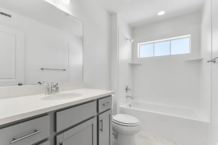 Vanity with light gray shaker cabinetry, engineered stone countertop, and a wide rectangular mirror
