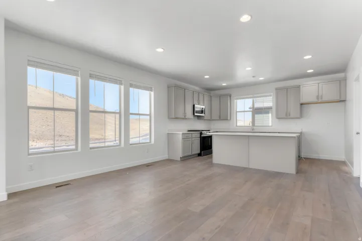 Open-concept kitchen and living area featuring wood-finish flooring, recessed lighting, and a kitchen island with a double basin sink