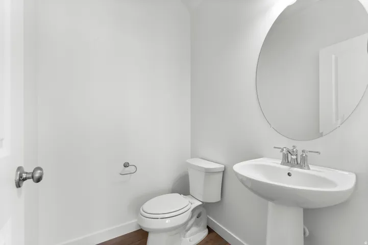 Pedestal sink with chrome faucet, circular wall mirror, and wood-finish flooring