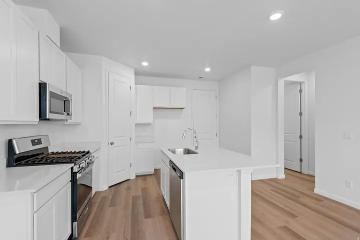 Kitchen featuring white cabinetry, stainless steel appliances, a center island with a sink, light-toned countertops, and wood-finish flooring