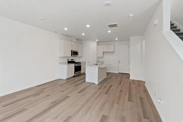 Open-concept living space featuring wood-finish flooring, recessed lighting, and a kitchen with an island, light cabinetry, and stainless steel appliances
