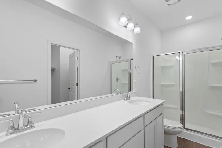 Dual vanity with integrated sinks, chrome fixtures, a full-width mirror, and a glass-enclosed shower