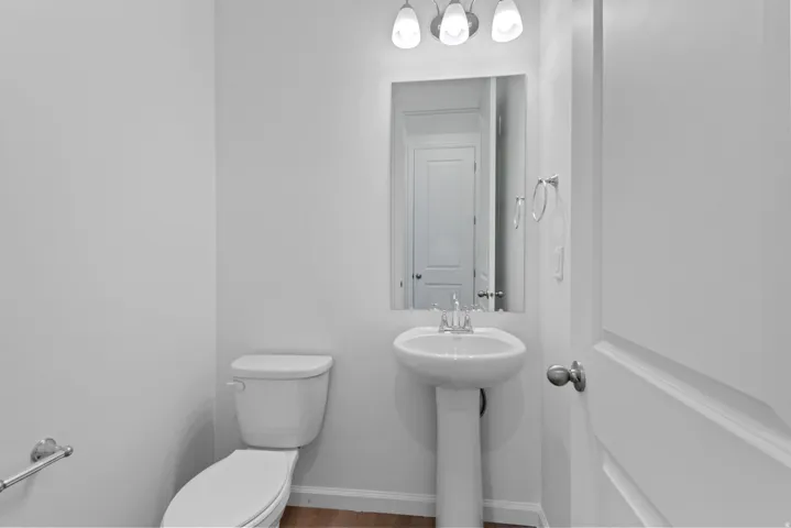 Pedestal sink with chrome faucet, wall-mounted mirror, and overhead vanity lighting