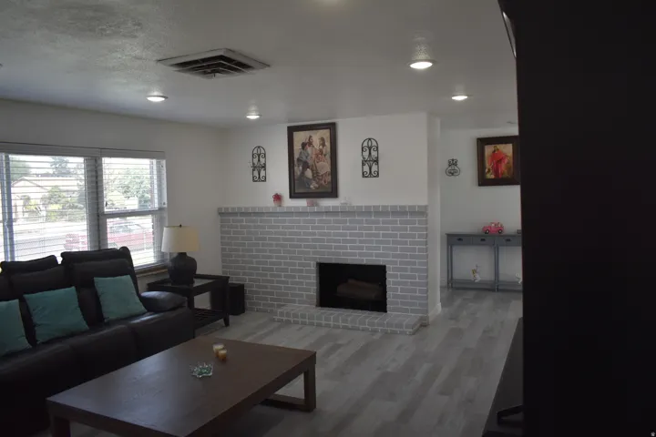 Living area featuring a painted brick fireplace, recessed lighting, wood-finish flooring, and white window blinds