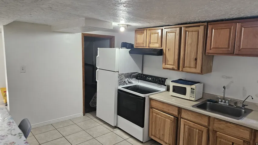Kitchen featuring wood cabinetry, white appliances, and tiled flooring