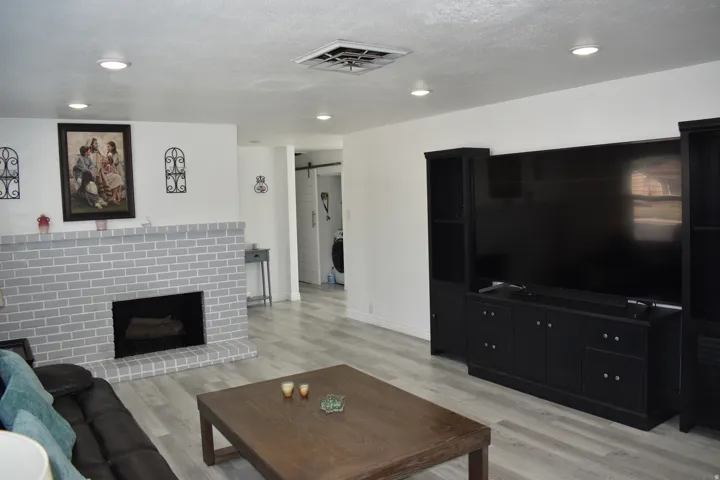 Spacious living area featuring light wood-finish flooring, a painted brick fireplace, and recessed lighting