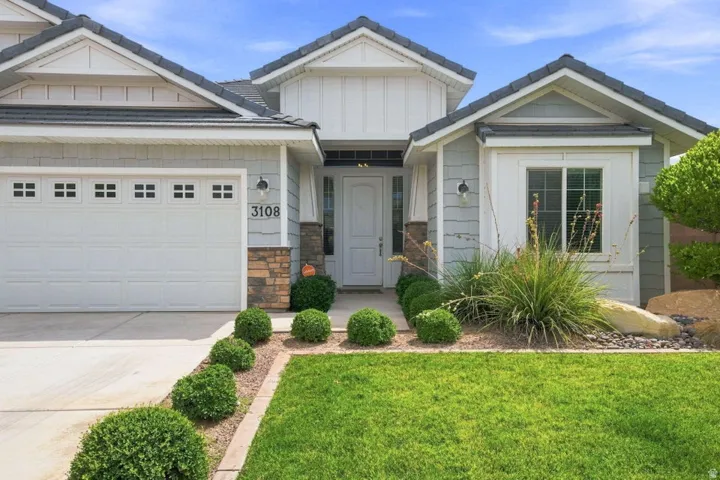 Gray shingle siding with white trim, stone accents, attached two-car garage, manicured lawn, and established landscaping