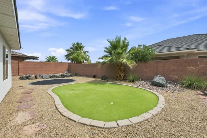 Resort-style backyard oasis featuring a manicured synthetic putting green with concrete edging, mature palm trees, decorative rock landscaping, and brick paver patio