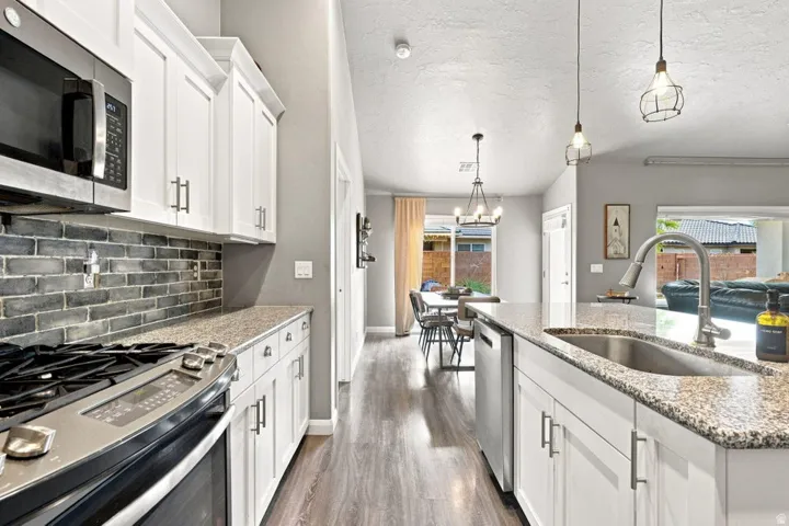 Kitchen featuring white cabinetry, stainless steel appliances, a brick-patterned backsplash, and wood-finish flooring
