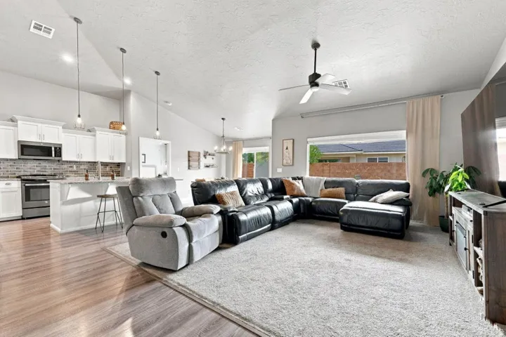 Vaulted ceilings, wood-finish flooring, white cabinetry, stainless steel appliances, and a ceiling fan with light fixture