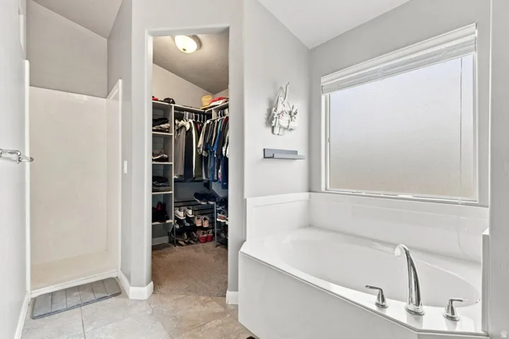 Walk-in shower with tile flooring, deep soaking tub with chrome fixtures, and a dedicated walk-in closet with built-in shelving