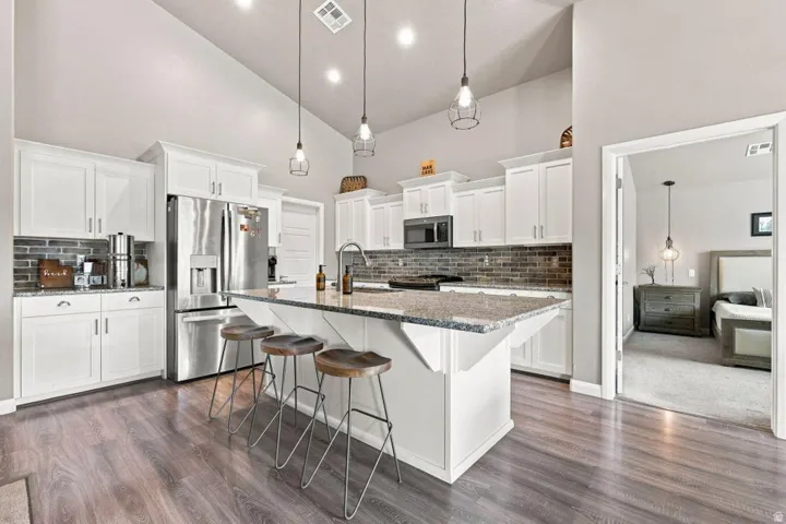 Kitchen featuring white cabinetry, stainless steel appliances, a center island with countertop seating, and wood-finish flooring