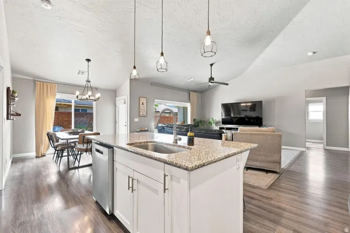 White kitchen island with a built-in stainless steel dishwasher, granite countertop, and undermount sink