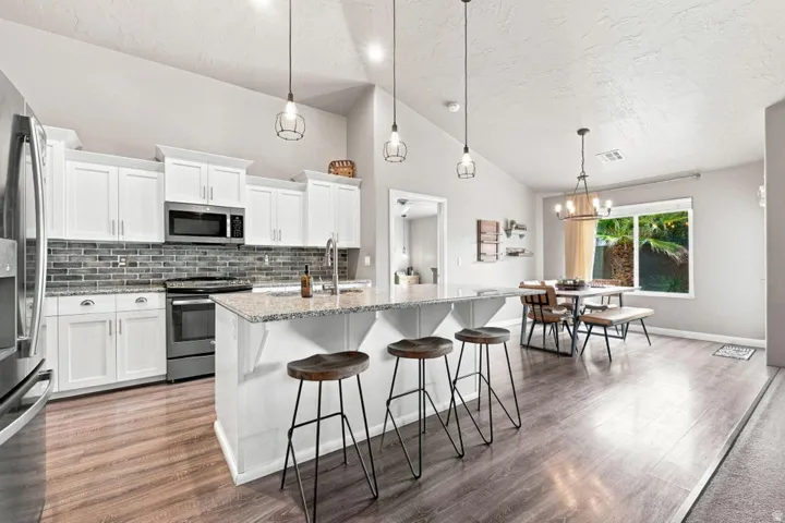 Kitchen featuring white cabinetry, stainless steel appliances, a tile backsplash, and a central island with a granite-finish countertop