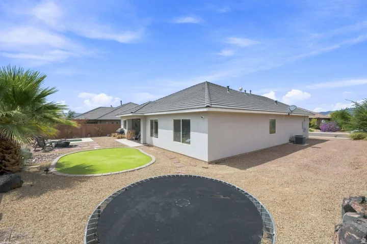 Rear exterior with a concrete tile roof, stucco siding, a stone patio, and a putting green