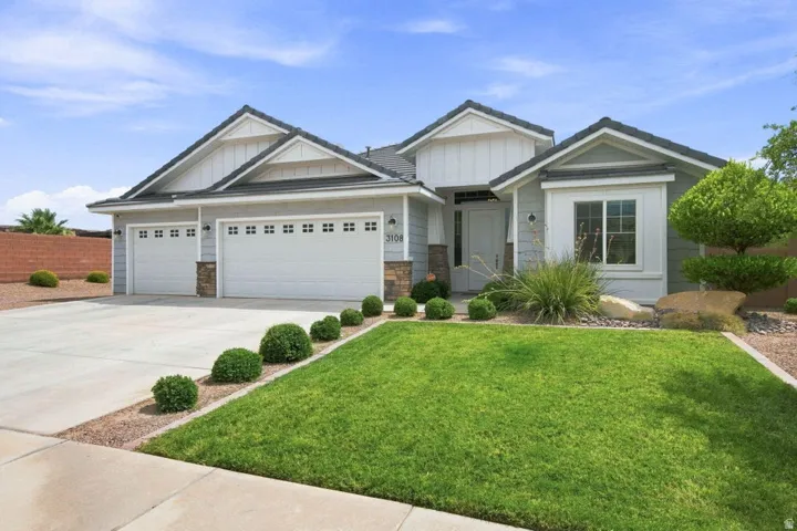 Light gray siding exterior with stone accents, a two-car garage, a covered entry, a bay window, and a manicured lawn