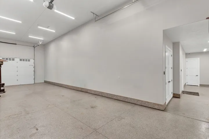 Spacious garage with an epoxy-coated concrete floor, white panel garage door, recessed lighting, and white interior doors