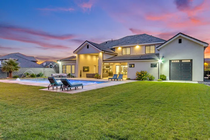 Expansive backyard featuring a manicured lawn, a swimming pool with fountain features, and a spacious patio area