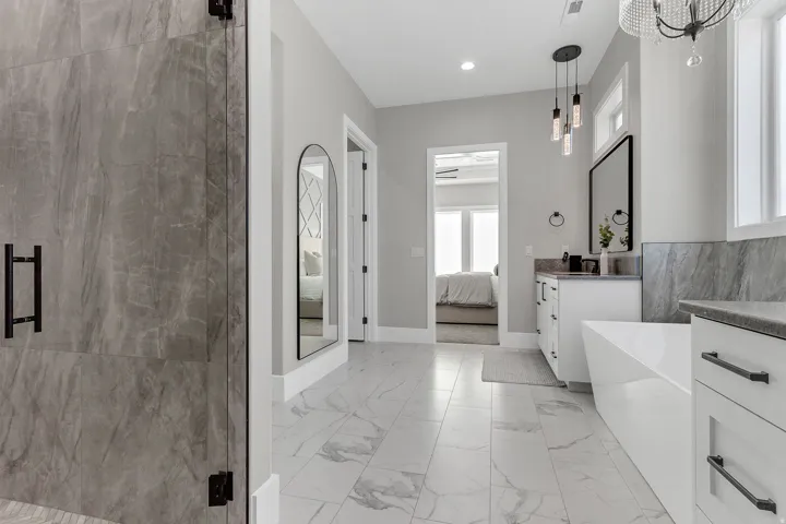 Walk-in shower with full-height stone-look tile, white freestanding soaking tub, dual vanity with undermount sinks, and plank-style tile flooring