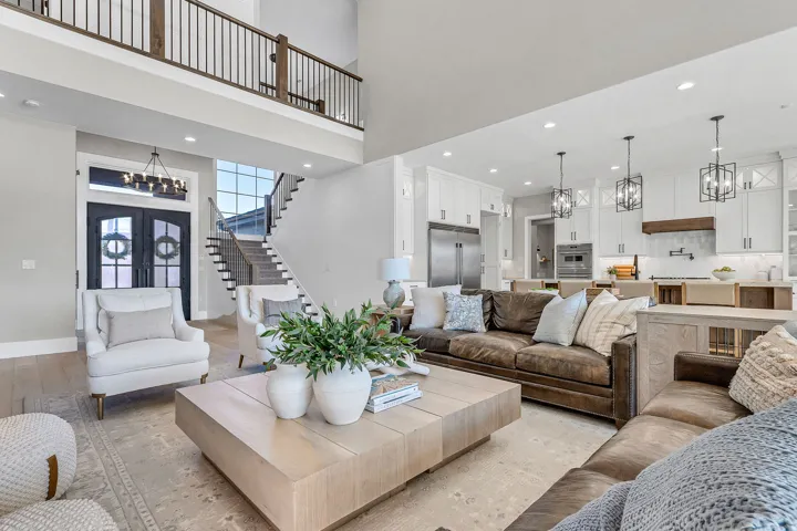 Open-concept living space featuring high ceilings, wood-finish flooring, a kitchen with white cabinetry and stainless steel appliances, and a two-story entryway with a grand staircase