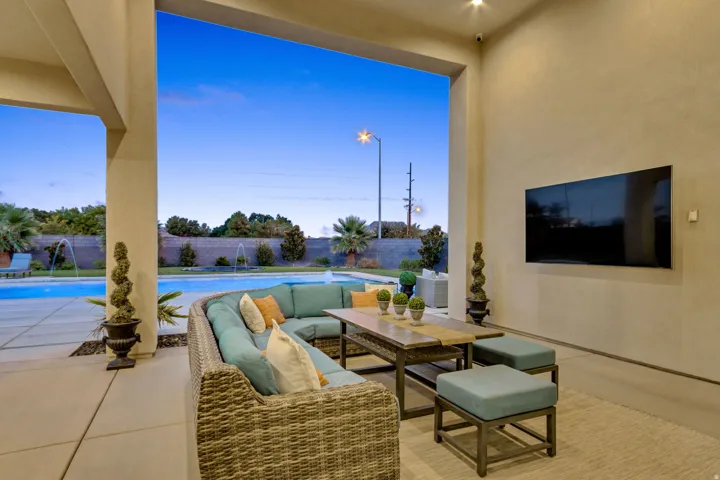 Covered outdoor living area with a built-in entertainment wall, recessed lighting, and direct access to a swimming pool with multiple water features