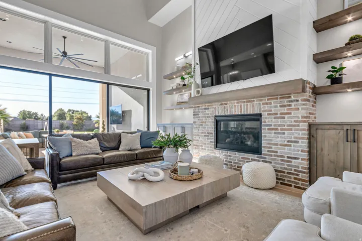 Vaulted ceiling with an exposed beam, a full-height brick fireplace with a wood mantle, custom built-in cabinetry, and expansive windows