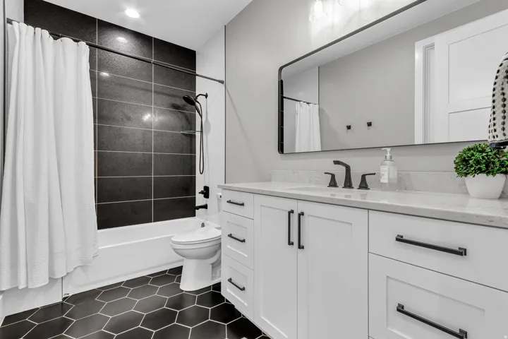 Bathroom featuring hexagon floor tiling, white vanity with black hardware, rectangular mirror, and black wall-mounted faucet
