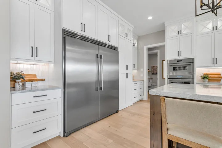 Stainless steel appliances, white shaker-style cabinetry, light wood-finish flooring, undermount lighting, and marble-look countertops