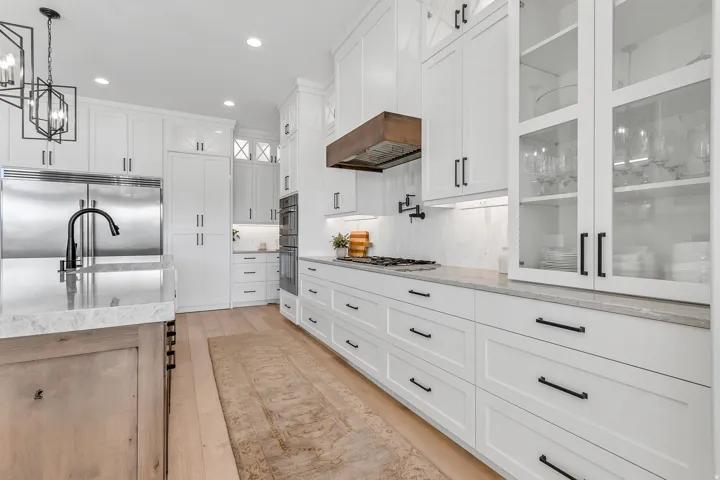 Stainless steel appliances, white cabinetry with black hardware, wood-finish flooring, light-toned countertop surfaces, and an integrated range hood