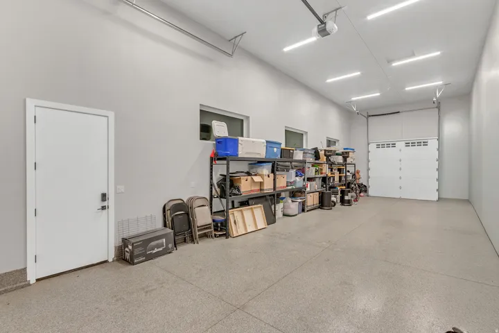 Spacious garage featuring a sectional overhead door, high ceilings, multiple linear LED light fixtures, and a white access door