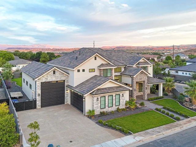 Contemporary exterior featuring a stone and stucco facade, multi-level tiled roofing, a covered entry with columns, multiple garages with dark doors, and structured landscaping