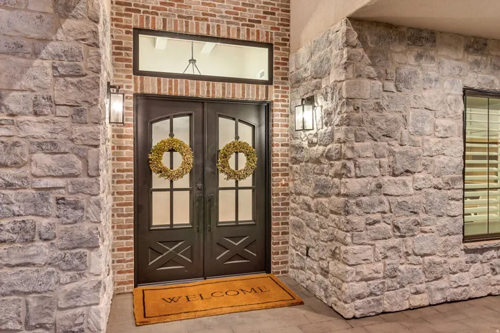 Double entry doors with transom window, brick facade, stone veneer accents, and exterior lighting fixtures