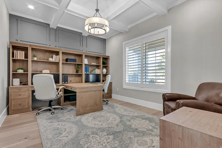 Wood-finish flooring, built-in wooden shelving, coffered ceiling, and a large window with plantation shutters