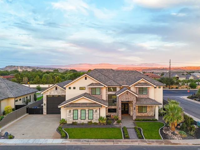 Stucco exterior with stone accents, dark tile roof, paved driveway, two-car garage, and established landscaping