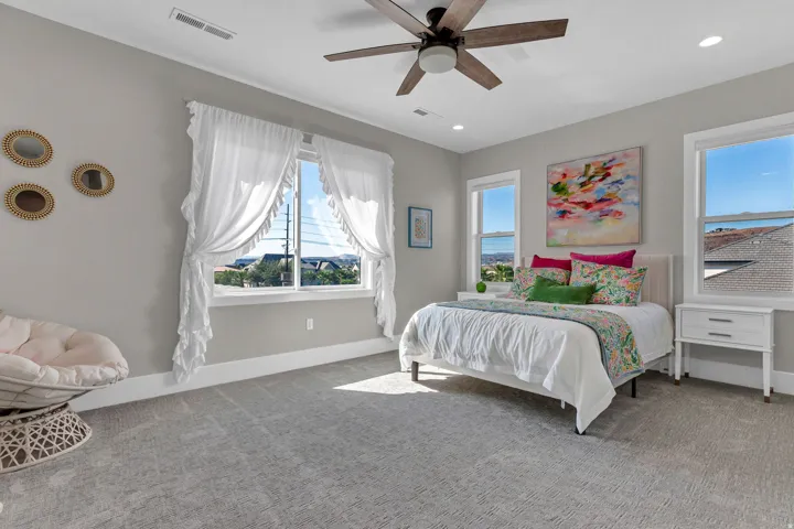Plush gray carpeting, a ceiling fan with integrated lighting, and multiple windows providing natural illumination