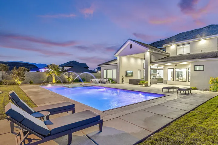 Resort-style backyard featuring a large swimming pool with water features, expansive concrete decking, and a covered patio